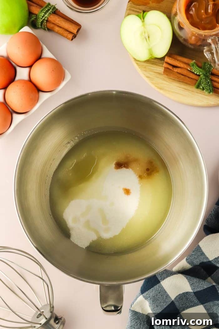 The foundational wet ingredients for the Bundt cake batter — oil, sugar, and vanilla extract — are expertly combined in a shiny metal mixing bowl, ready for eggs.