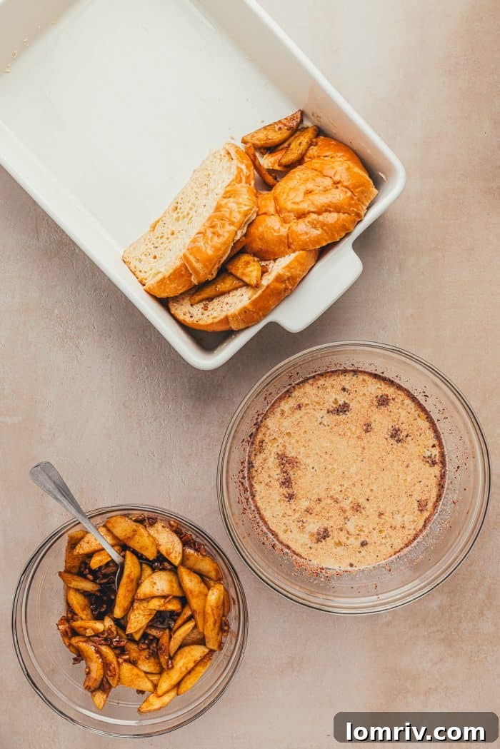 A white baking dish with freshly dipped croissants and a bowl of apple pie filling and french toast egg mixture.
