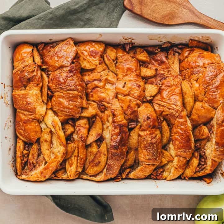 A white dish with baked croissant french toast with apples.