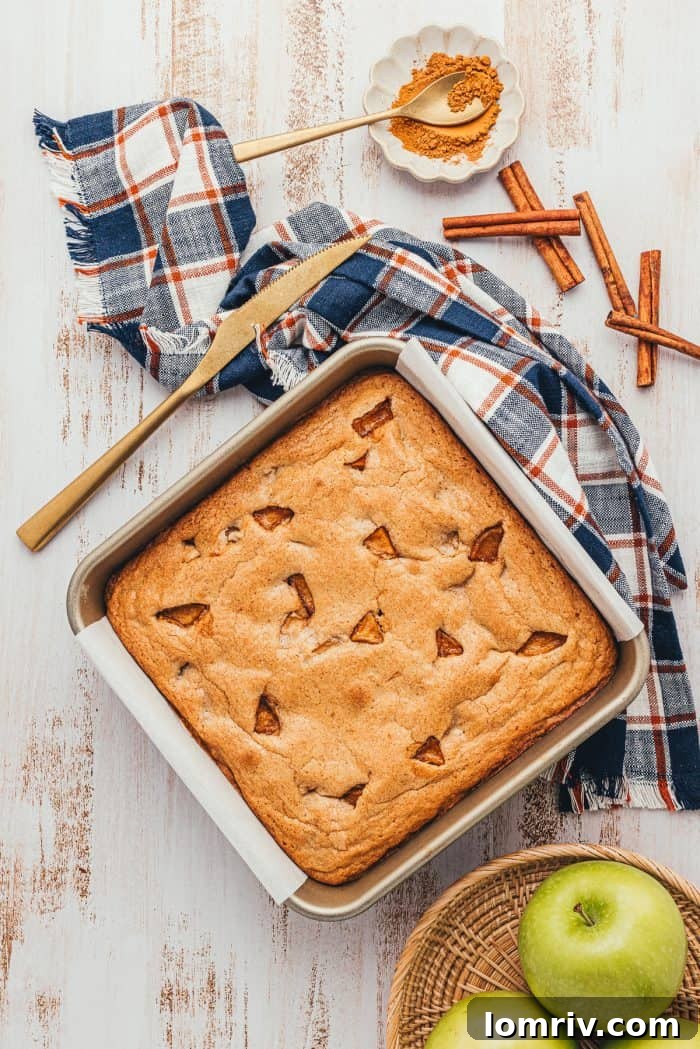 A square baking pan with baked apple pie blondies and a bowl of green apples.