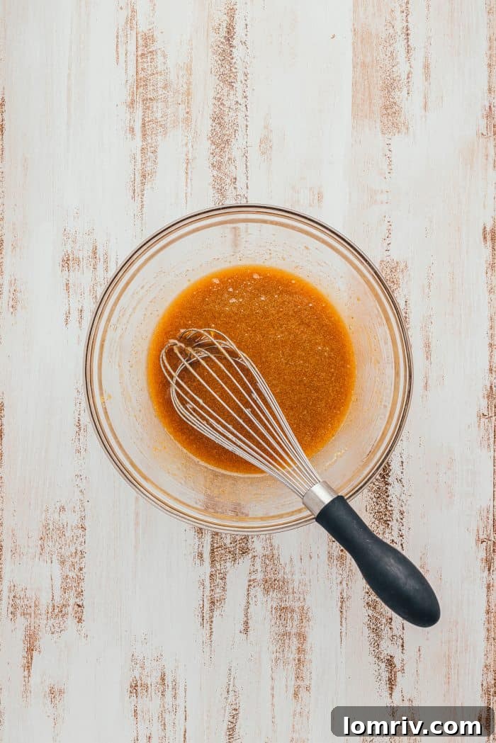 A glass bowl with the wet ingredients for Apple Blondies and a whisk.