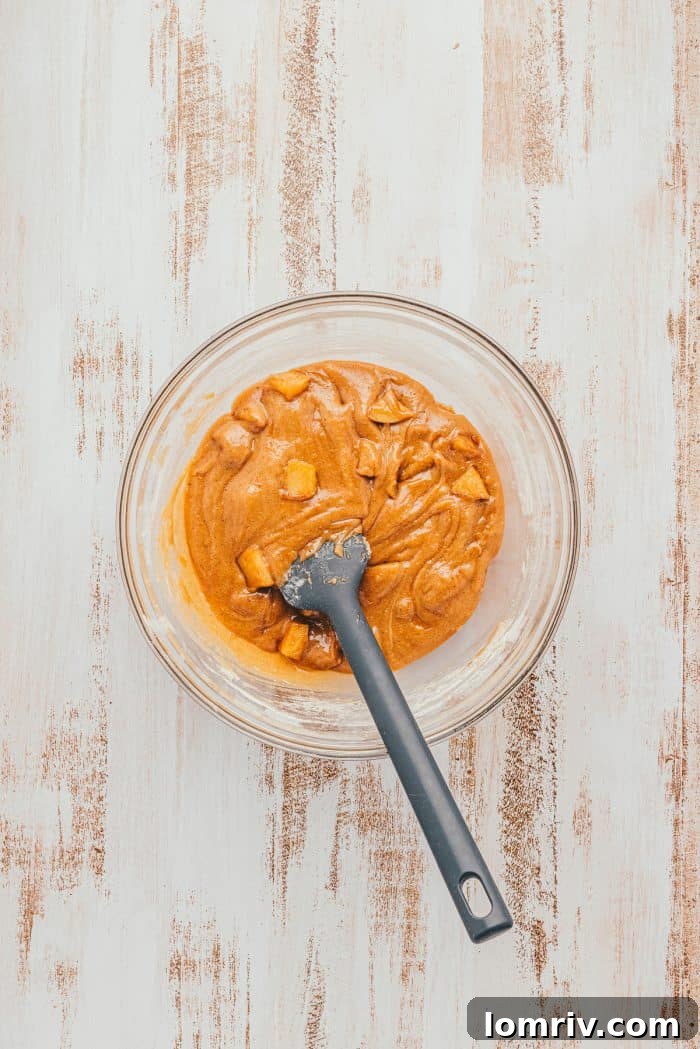 The batter for Apple Blondies with cubed apple in a glass bowl with a spatula.