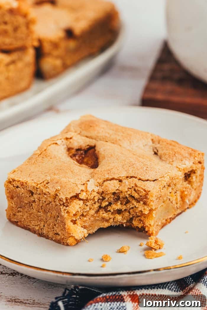 A slice of Apple Blondie with a bite taken out of it on a white plate.