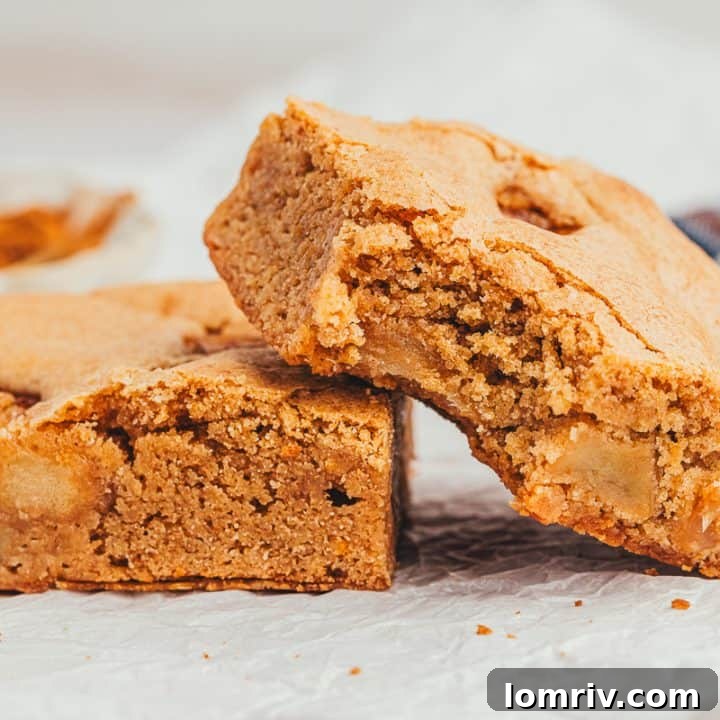 Two apple pie blondies beside themselves and one has a bite taken out of it.