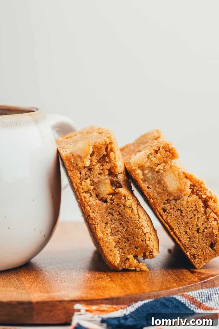 Two apple pie blondies leaning against a cup of coffee.