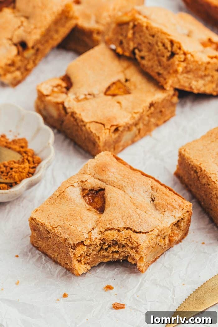 A few apple pie blondies scattered on a counter with one Blondie with a bite out of it.