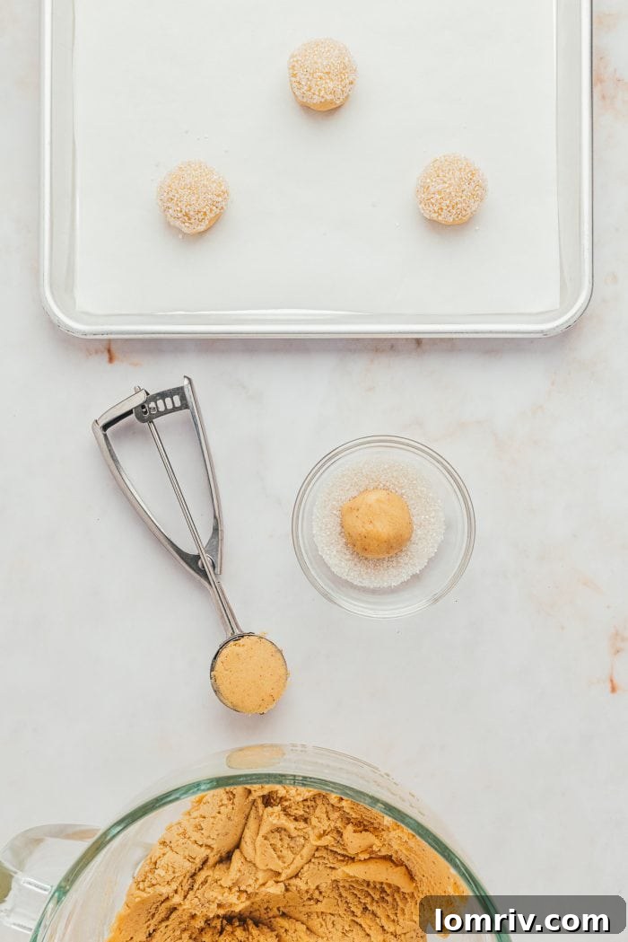 A small glass bowl filled with sparkling sanding sugar sits beside a cookie sheet with perfectly formed balls of cookie dough.