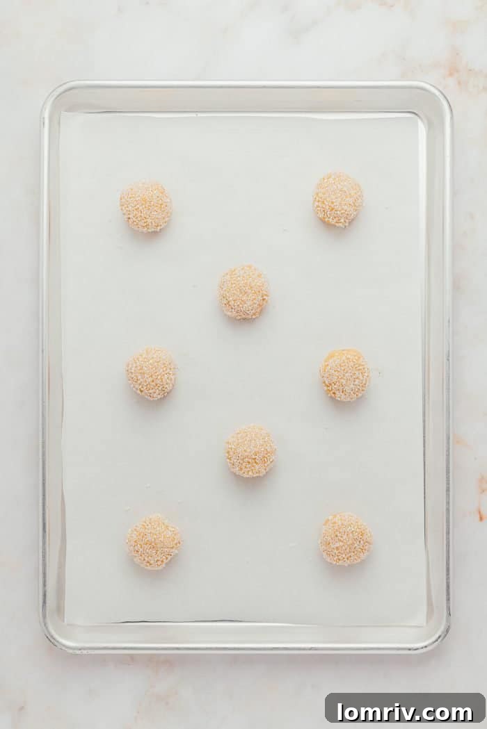 A cookie tray laden with various balls of raw sugar cookie dough, each awaiting its transformation in the oven.