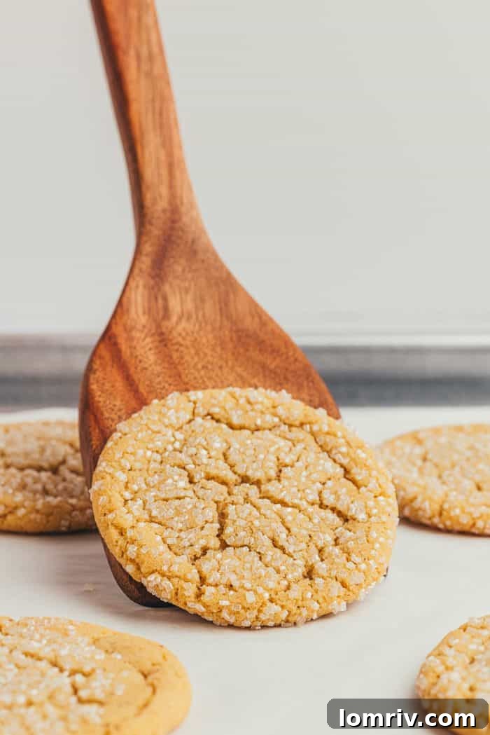 A wooden spatula carefully lifting a browned butter sugar cookie from a baking sheet, showcasing its delicate structure.