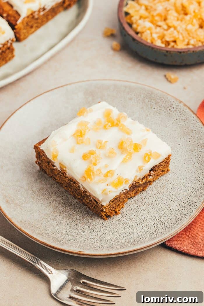 A gray ceramic plate featuring a single, beautifully frosted gingerbread bar, ready to be enjoyed. A fork lies delicately nearby.