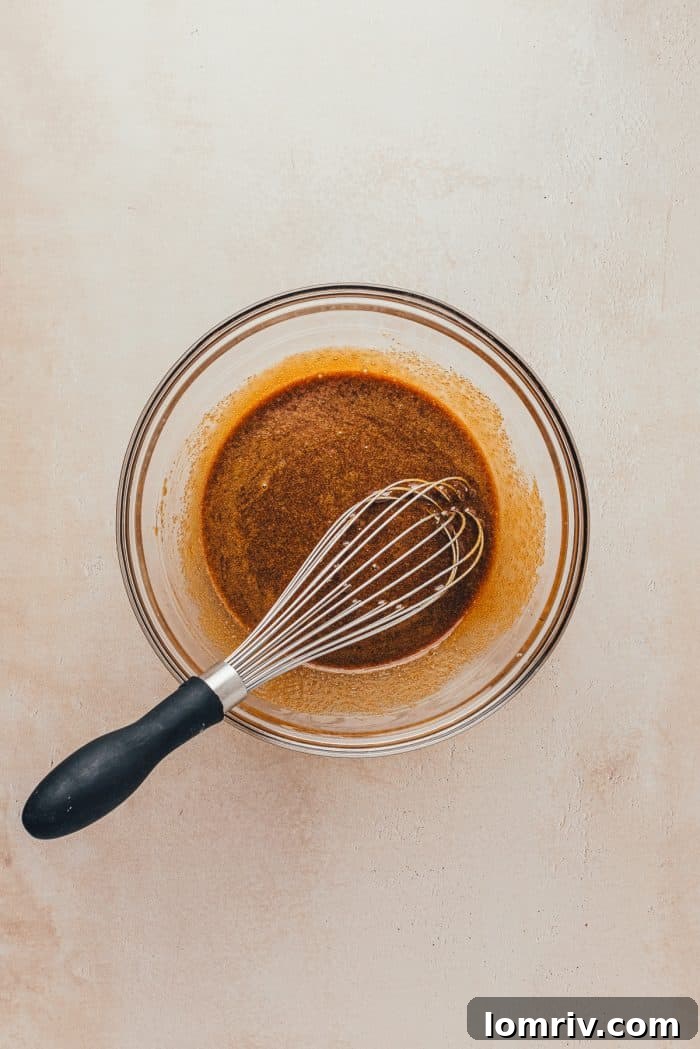 Wet ingredients for gingerbread bars: melted butter, molasses, egg, sugar, and vanilla, being whisked together in a glass bowl.