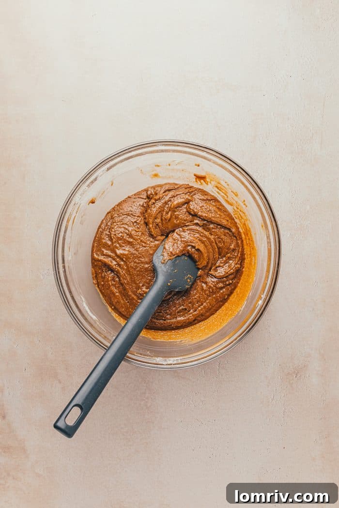 Thick gingerbread batter in a glass bowl, with a spatula ready to transfer it to the baking pan.