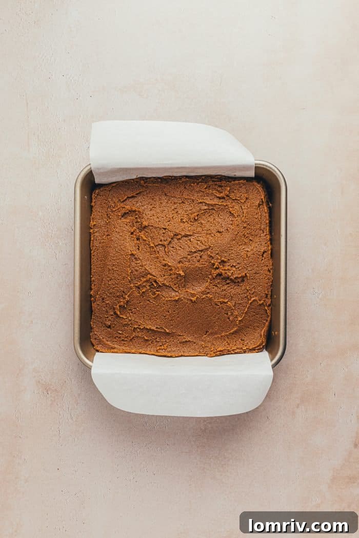 Raw gingerbread batter evenly spread in a baking pan lined with parchment paper, ready for baking.