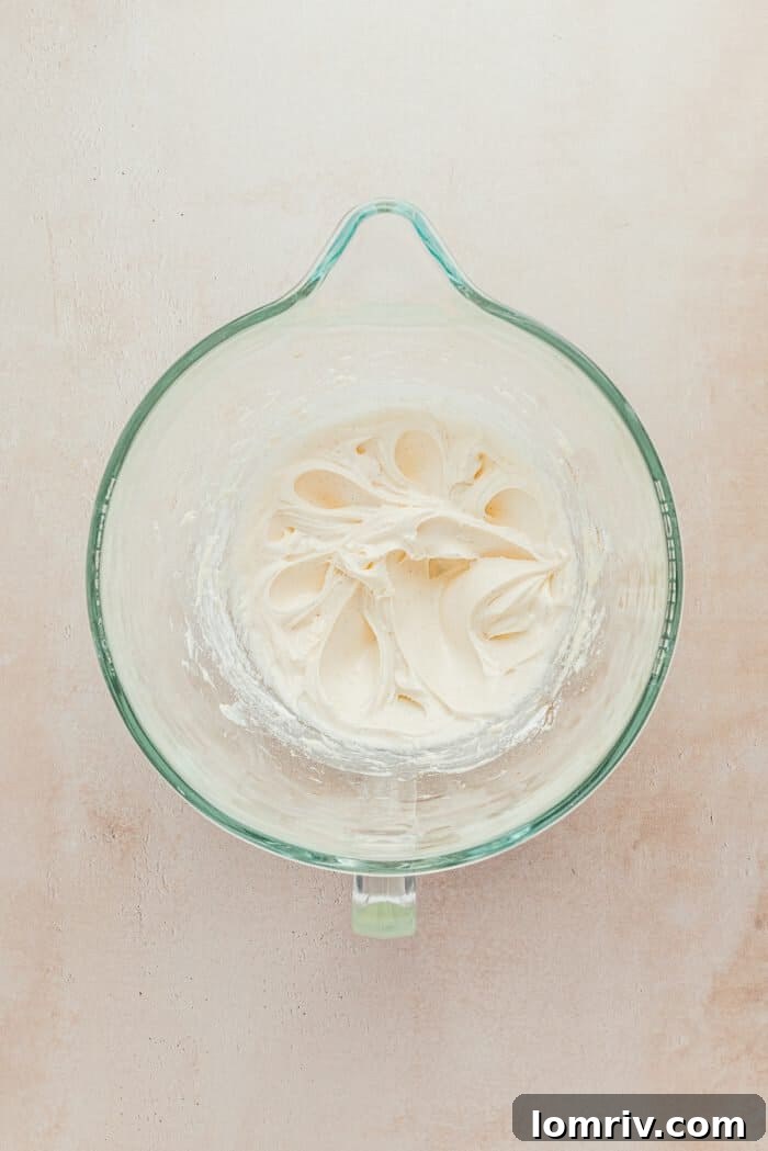 A glass mixing bowl filled with smooth, creamy cream cheese frosting, ready to be spread.