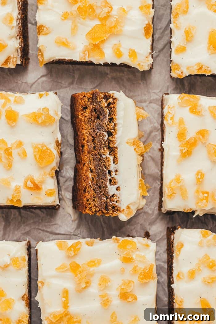A single square gingerbread bar with frosting and candied ginger, turned on its side to show the soft, dense texture of the bar.