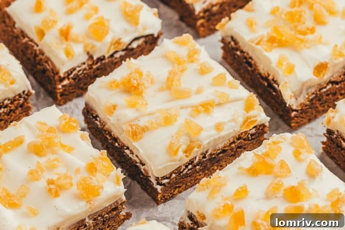 A plate of neatly cut frosted gingerbread bars with candied ginger on top, ready for serving.