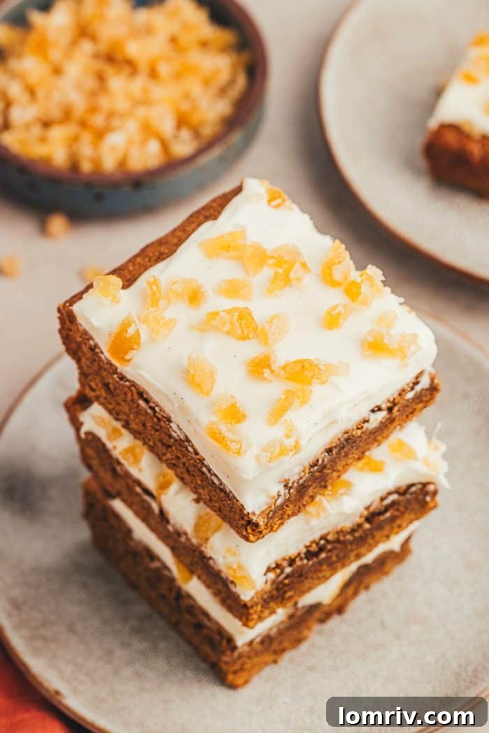 A beautifully arranged stack of three frosted gingerbread bars on a rustic gray plate, highlighting their inviting appeal.