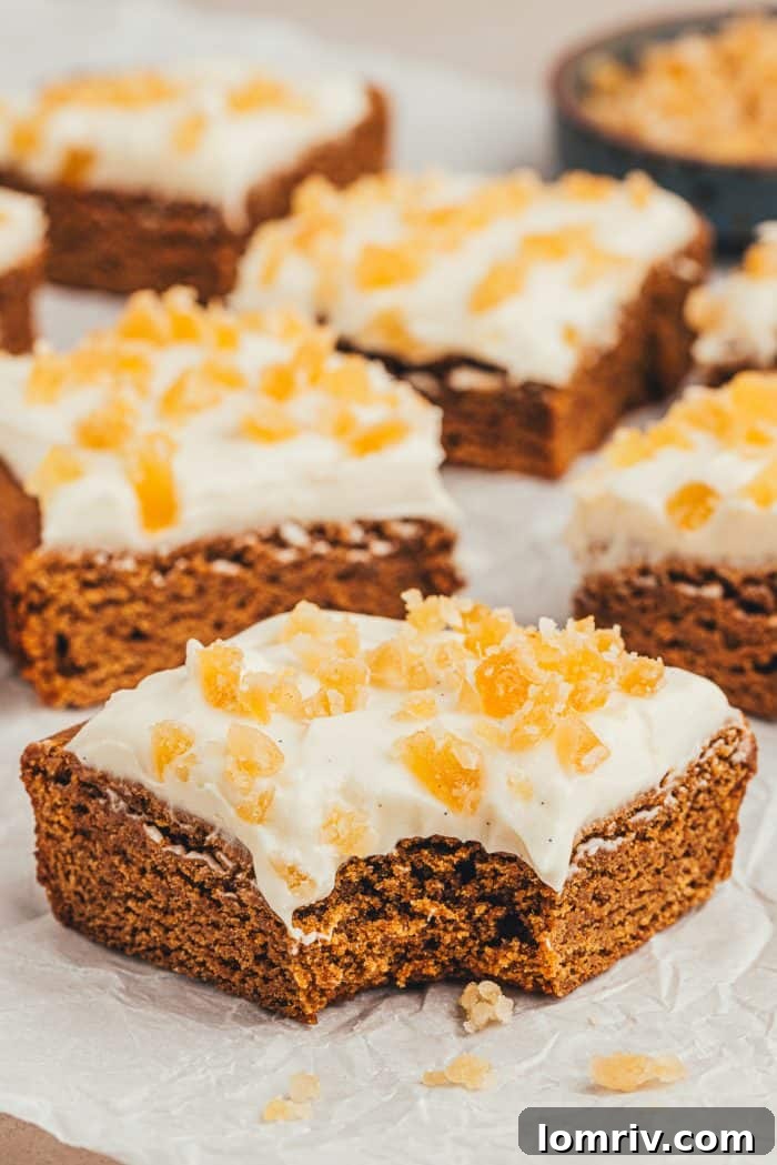 Several frosted gingerbread bars, cut into neat squares, arranged on a gray plate. One bar has a bite taken out, revealing its soft interior.