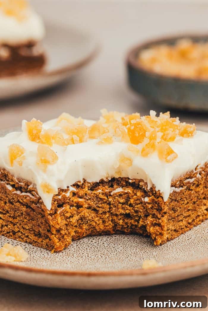 A close-up of a single frosted gingerbread bar with a bite taken, showing the rich, spiced cake texture and creamy white frosting.