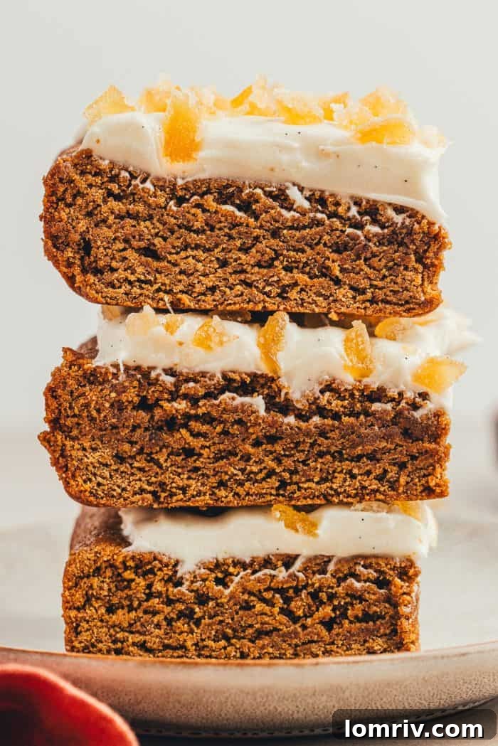 A stack of three frosted gingerbread bars sits invitingly on a grey plate, with a slightly blurred background creating a cozy atmosphere.