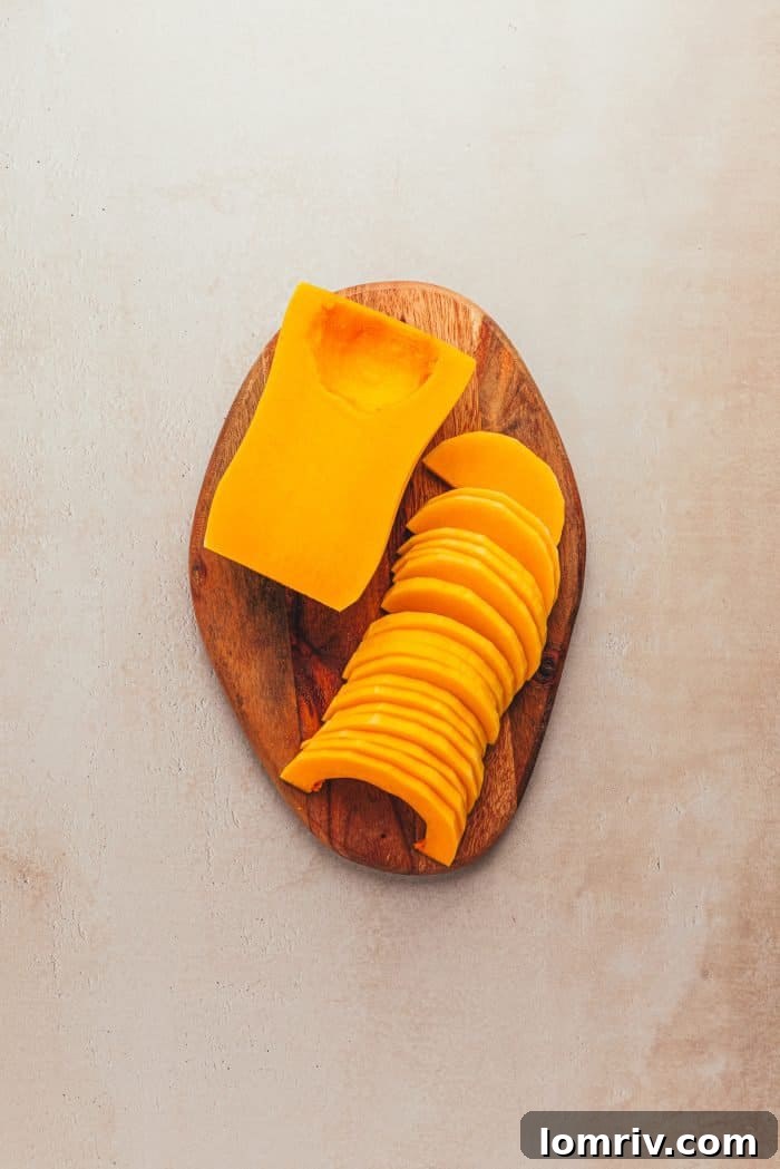 Peeled and thinly sliced butternut squash resting on a wooden tray, perfectly prepped.