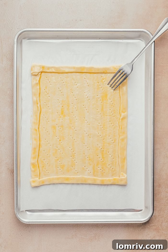 Puff pastry on a baking sheet with a formed crust, showing fork pricks inside the border for even baking.