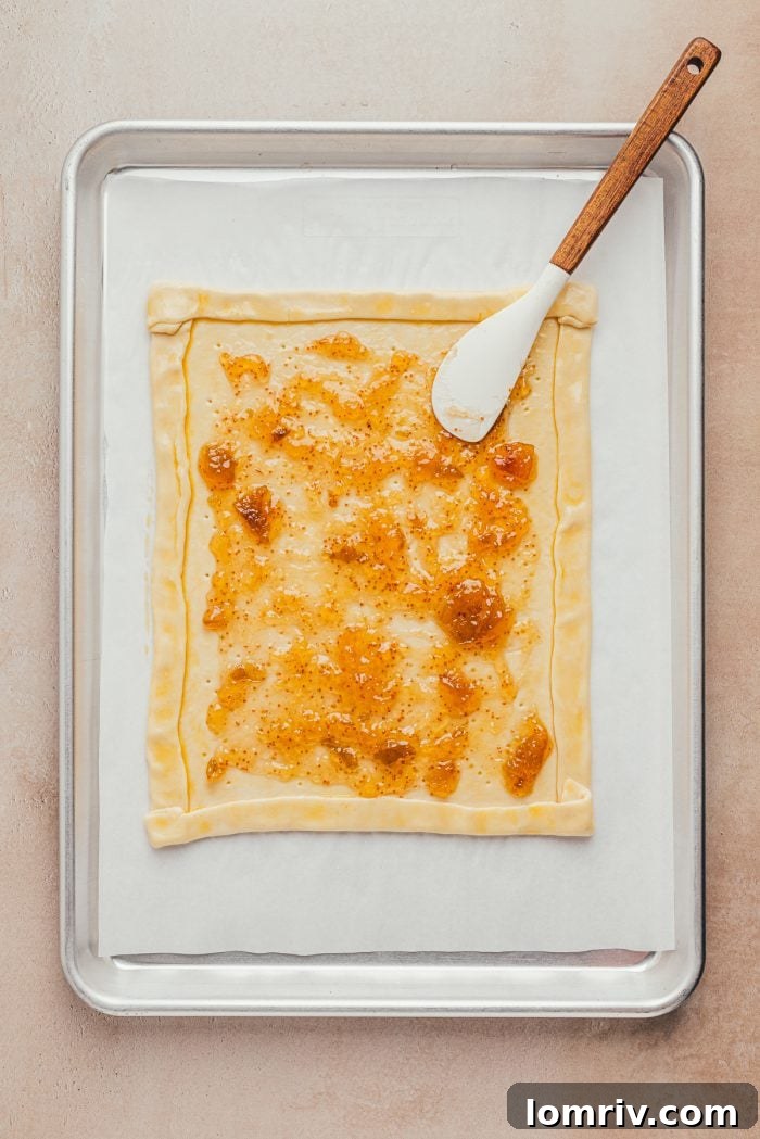 Fig jam thinly brushed over puff pastry with a defined crust on a baking sheet.