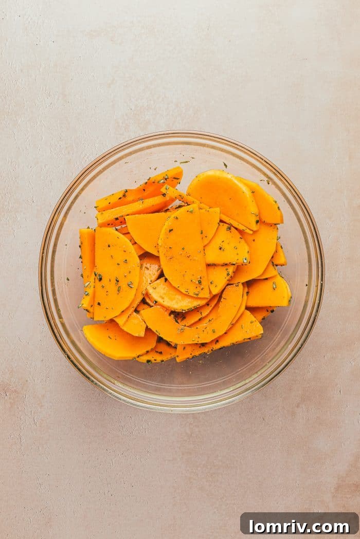 Thinly sliced butternut squash mixed with fresh herbs and olive oil in a clear glass bowl.