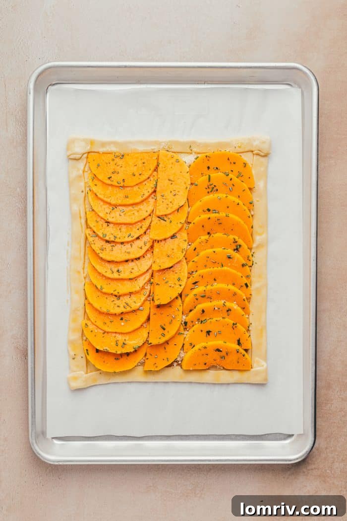 An unbaked butternut squash tart with layered slices, ready to go into the oven on a baking sheet.