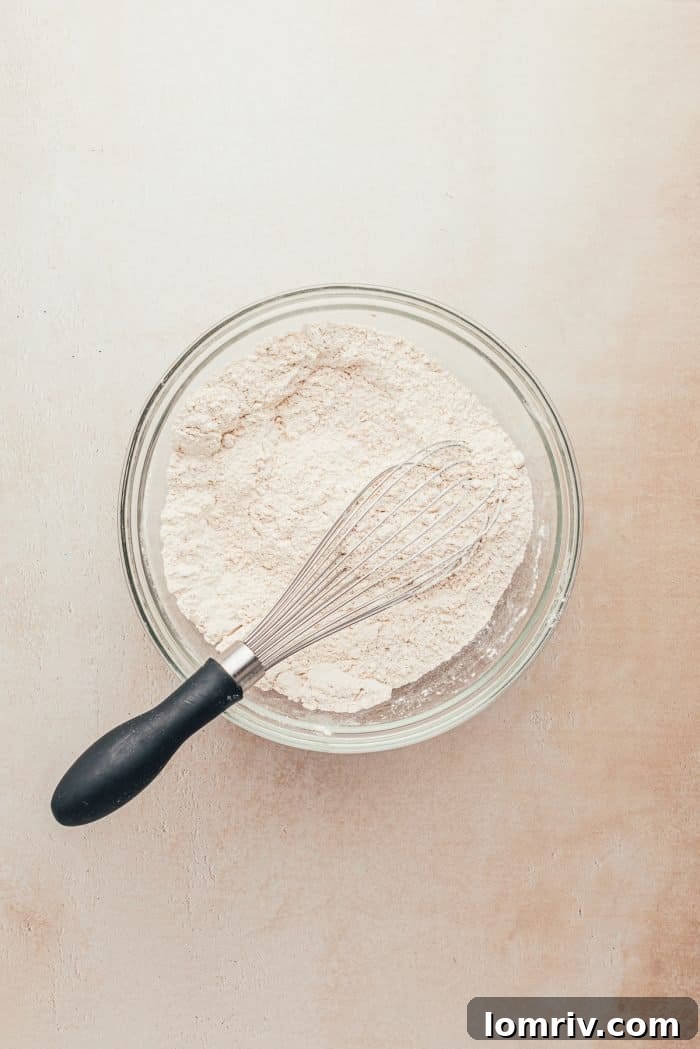 A glass bowl with all-purpose flour and a whisk, illustrating the process of mixing dry ingredients for baking.