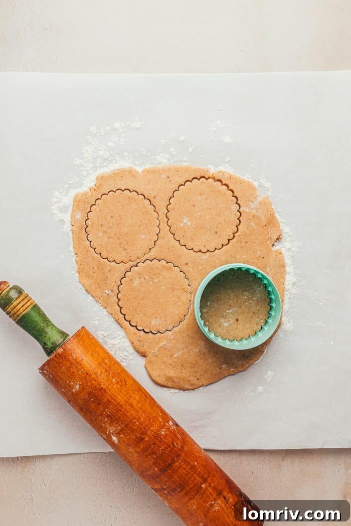 Cookie dough rolled out on parchment paper, with a round cookie cutter and rolling pin visible, ready for cutting.