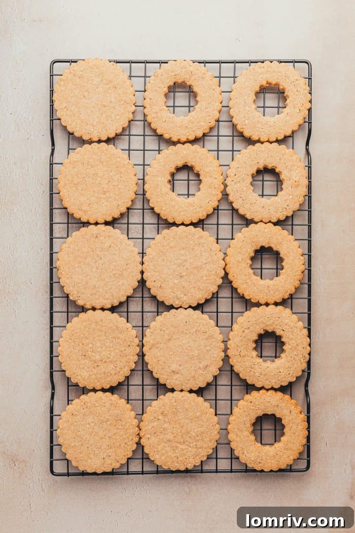 A cooling rack neatly filled with freshly baked Linzer cookie halves, some with cutouts, others solid, ready for assembly.
