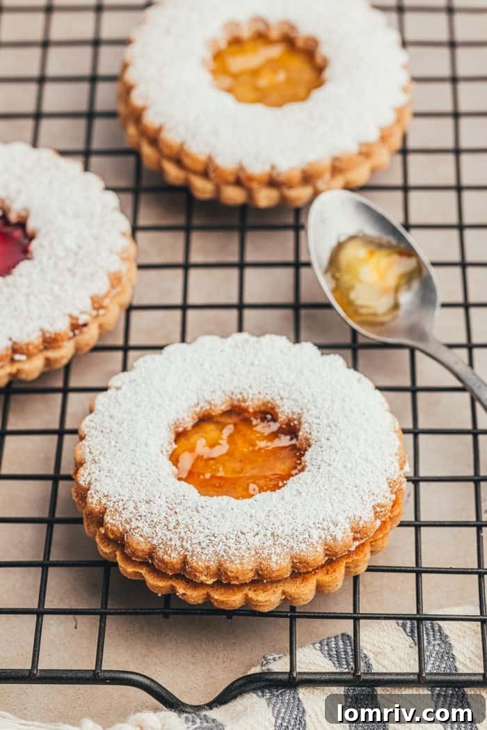 A cooling rack filled with baked Linzer cookies and a spoon ready to spread jam, illustrating the final steps of preparation.