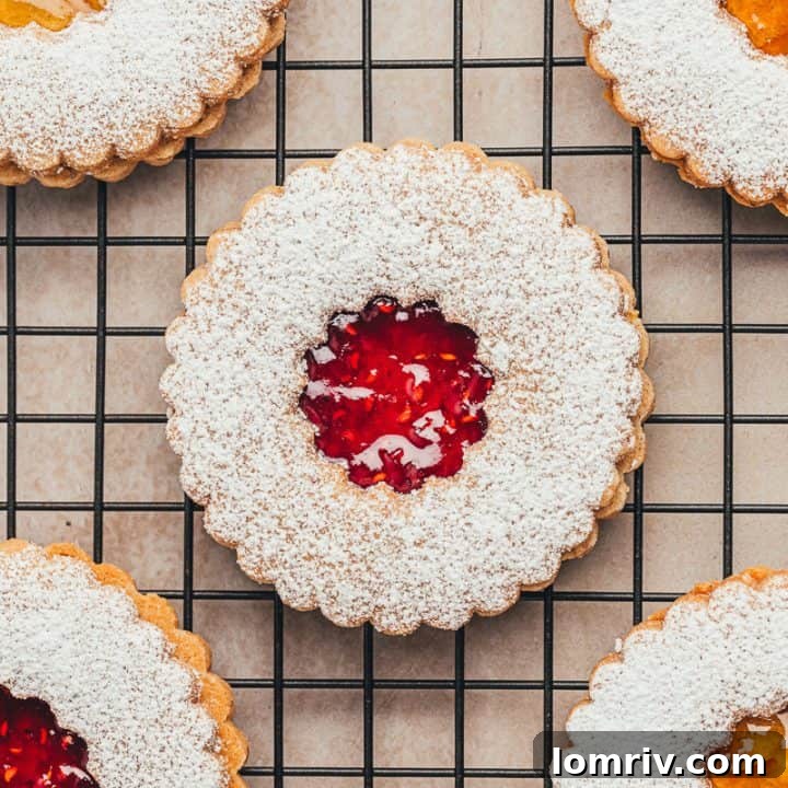 A cooling rack with Linzer cookies with powdered sugar and jam.