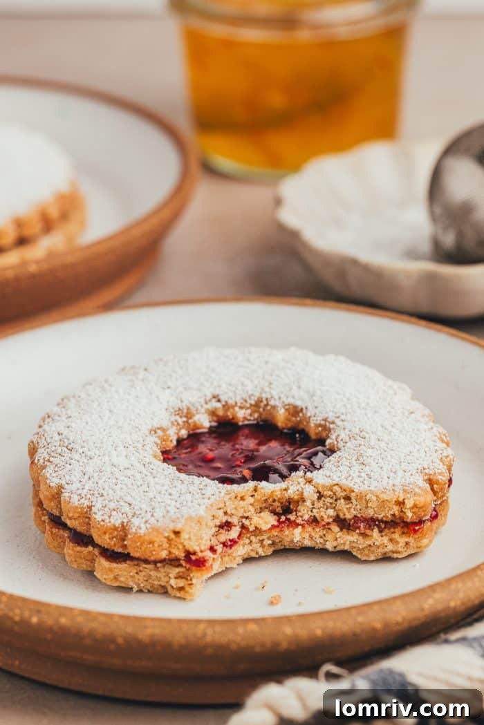 A close-up of a hazelnut Linzer cookie with a bite taken out, revealing the rich jam filling and crumbly texture.