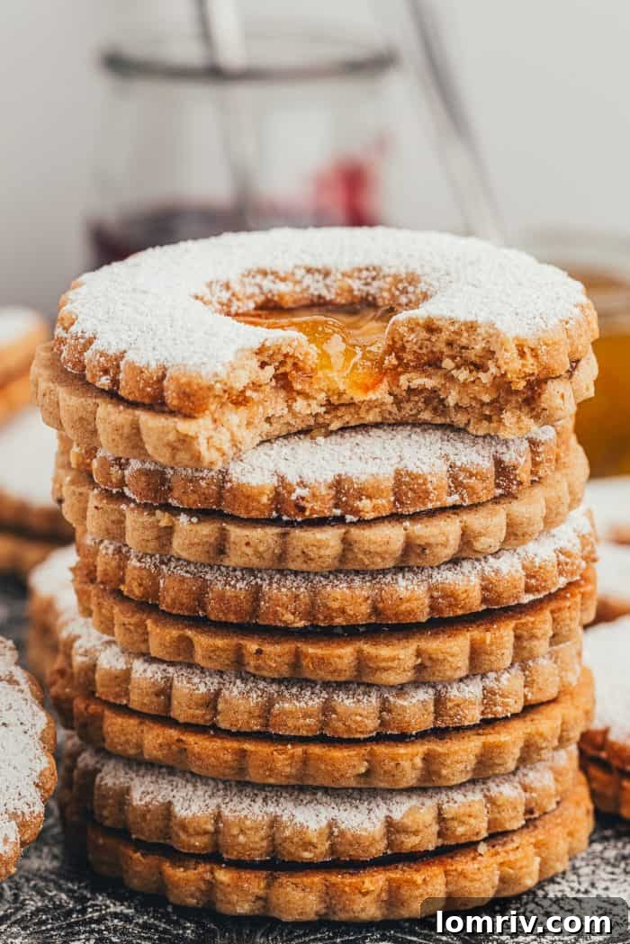 A stack of golden-baked Linzer cookies, one with a missing bite, showcasing the rich texture and delicious filling.