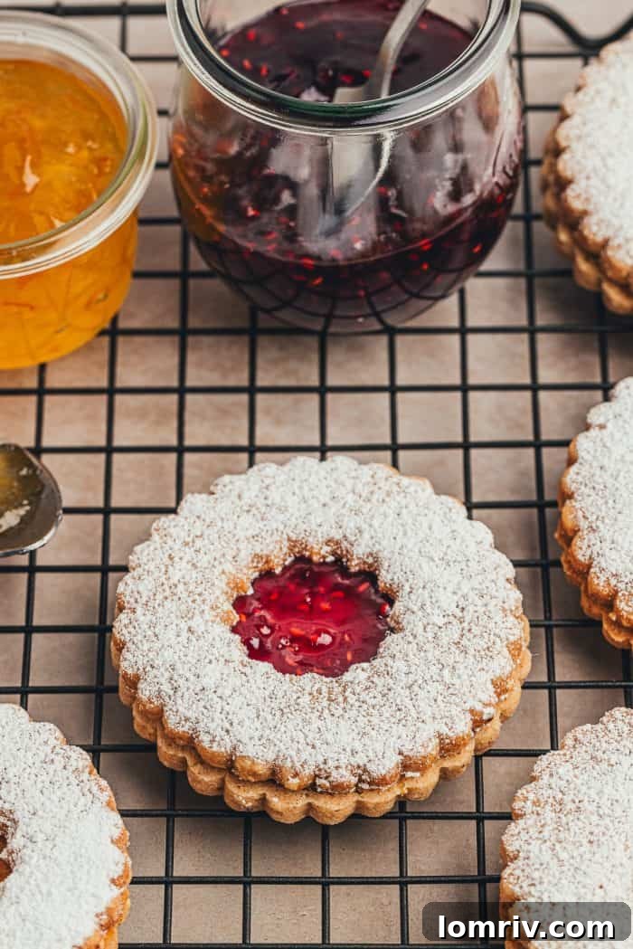 A cooling rack laden with baked hazelnut Linzer cookies, flanked by glass bowls brimming with various vibrant jams, ready for assembly.