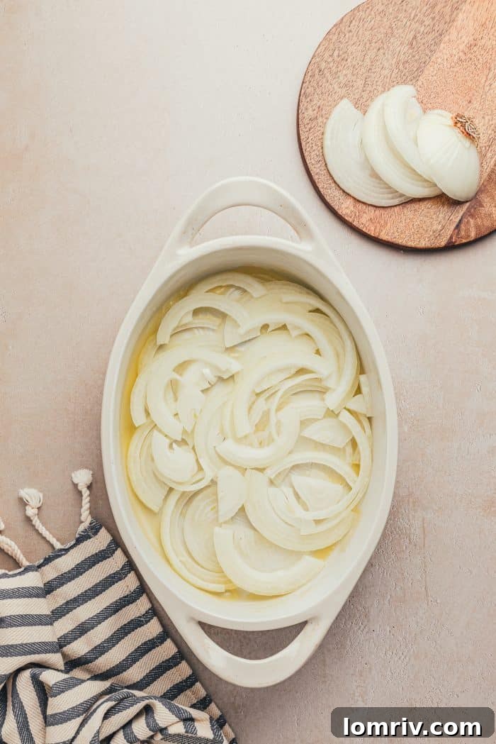 Sliced onions layered in a baking dish with butter
