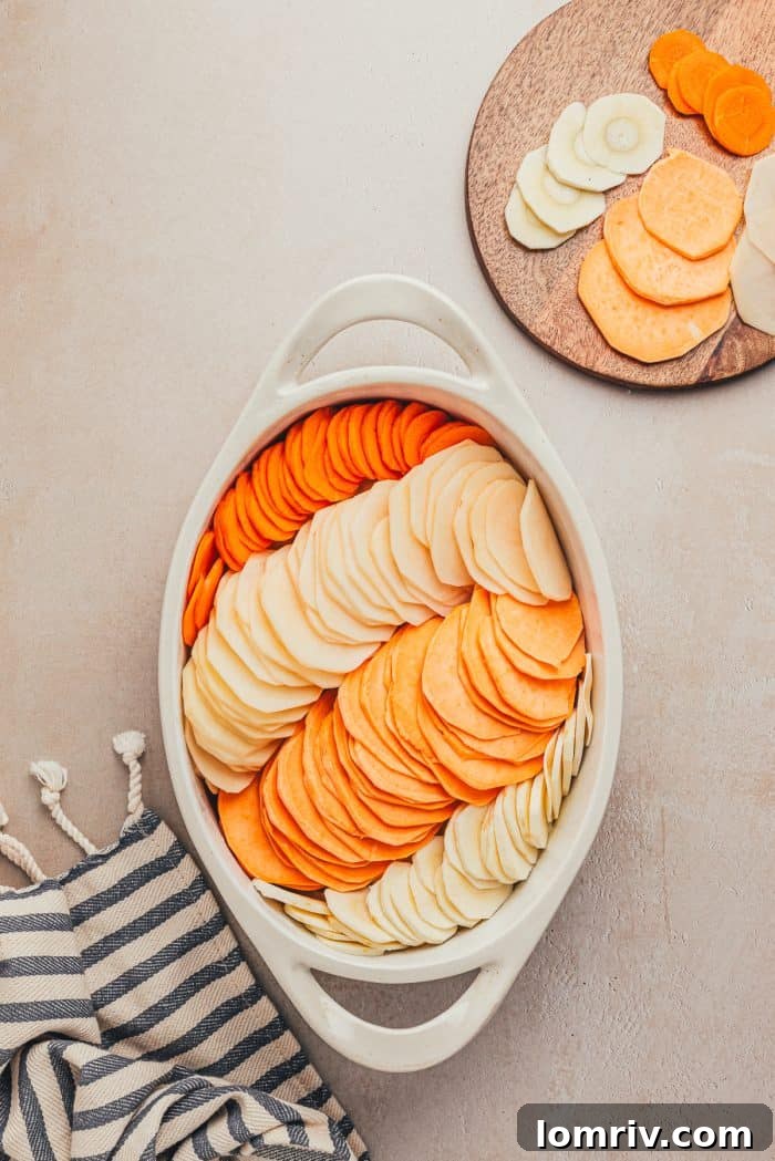 A variety of sliced root vegetables arranged in rows in a white baking dish.