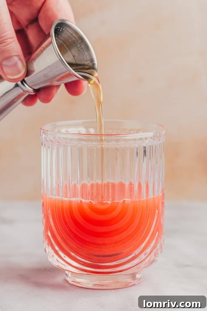 Rosemary honey syrup being drizzled into the blood orange and lime juice mixture.