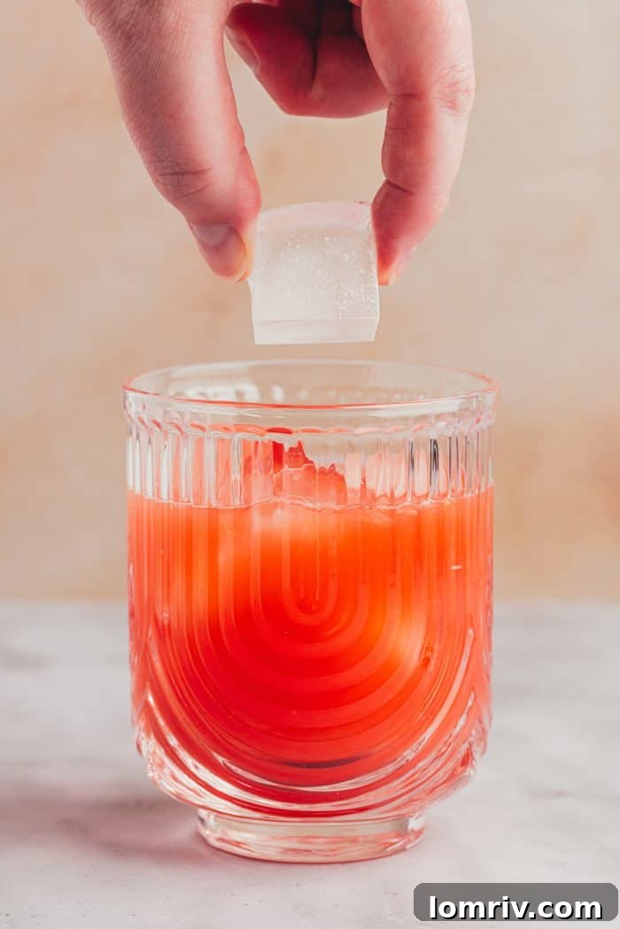 Ice cubes being dropped into the prepared blood orange mixture in a glass.