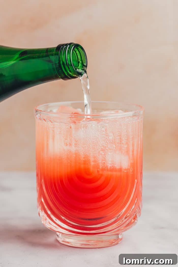 Sparkling water being poured into the glass, topping off the blood orange mocktail mixture.