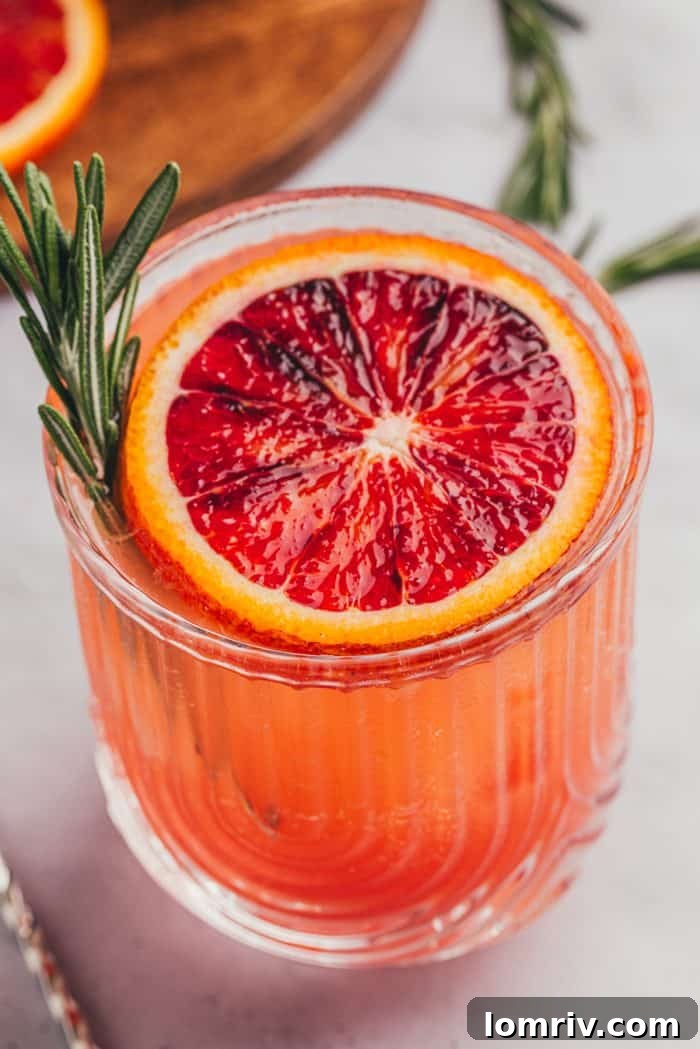 A finished blood orange mocktail, elegantly garnished with a blood orange slice and a rosemary sprig, ready for enjoyment.