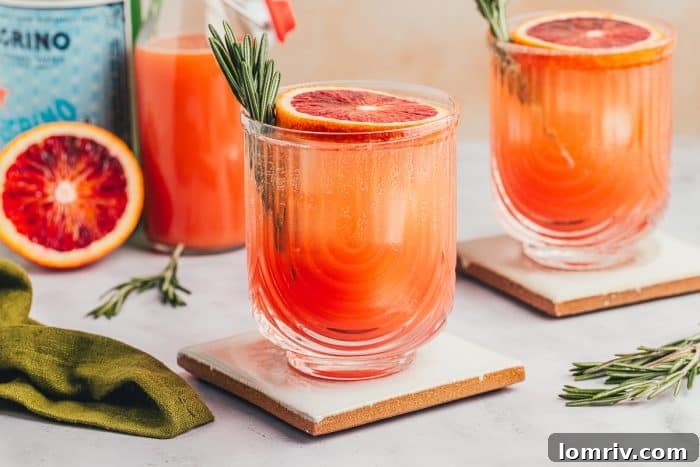 A stunning arrangement of three blood orange mocktails, artfully garnished with blood orange slices and rosemary sprigs, against a soft, blurred background.