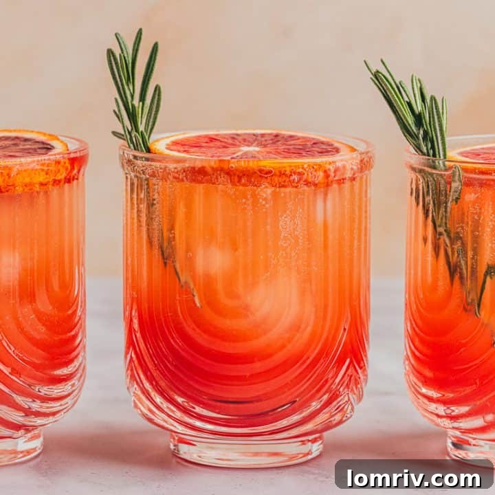 Three blood orange mocktails with slices of blood orange and sprigs of rosemary.