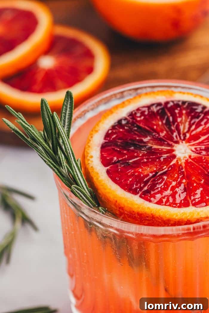 Close-up shot of a blood orange mocktail with sparkling water bubbles, a blood orange slice, and a rosemary sprig.