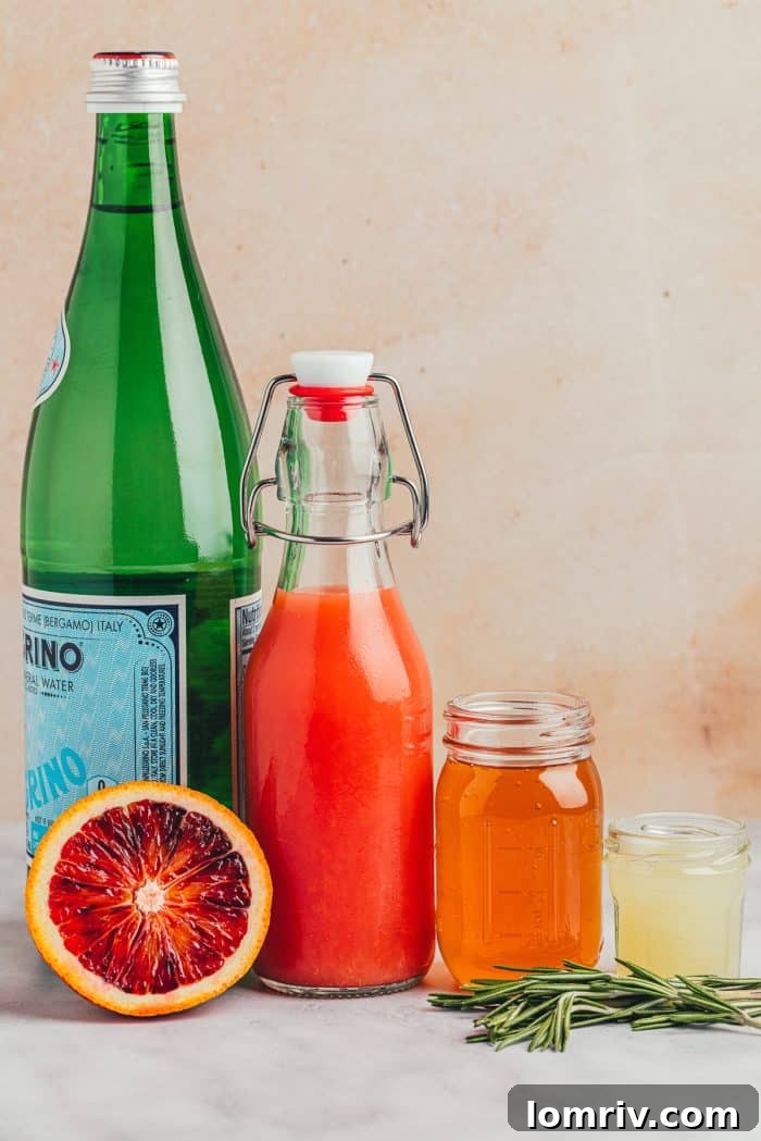 A flat lay photograph showcasing the key ingredients for the blood orange mocktail: honey, fresh rosemary sprigs, a bowl of blood oranges, and a bottle of sparkling water.