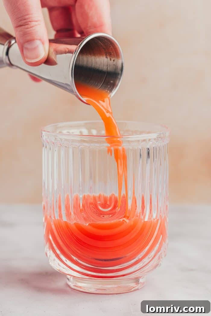 Freshly squeezed blood orange juice being poured into a serving glass.