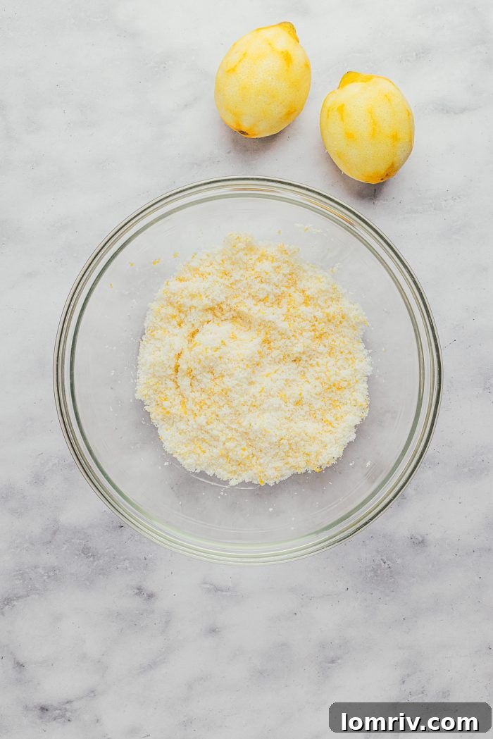 Granulated sugar and fresh lemon zest mixed in a clear glass bowl, showcasing the vibrant zest.