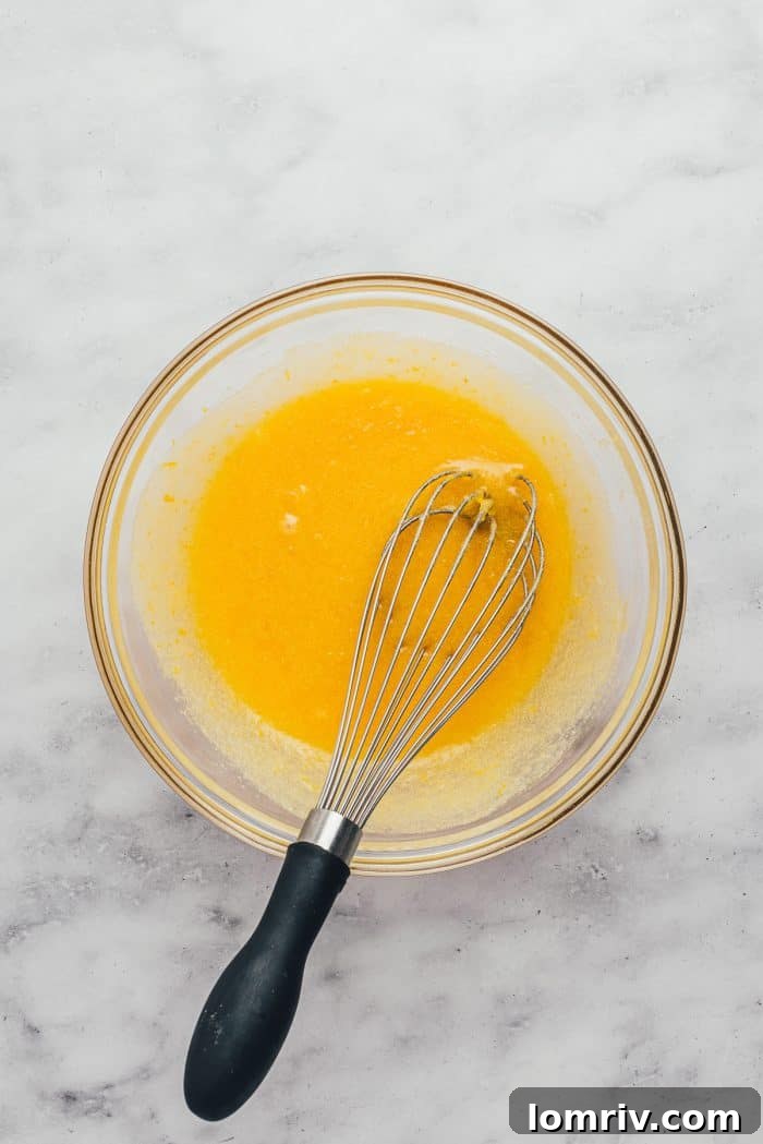A glass bowl containing the whisked wet ingredients for the blondies, including egg, lemon juice, and butter.
